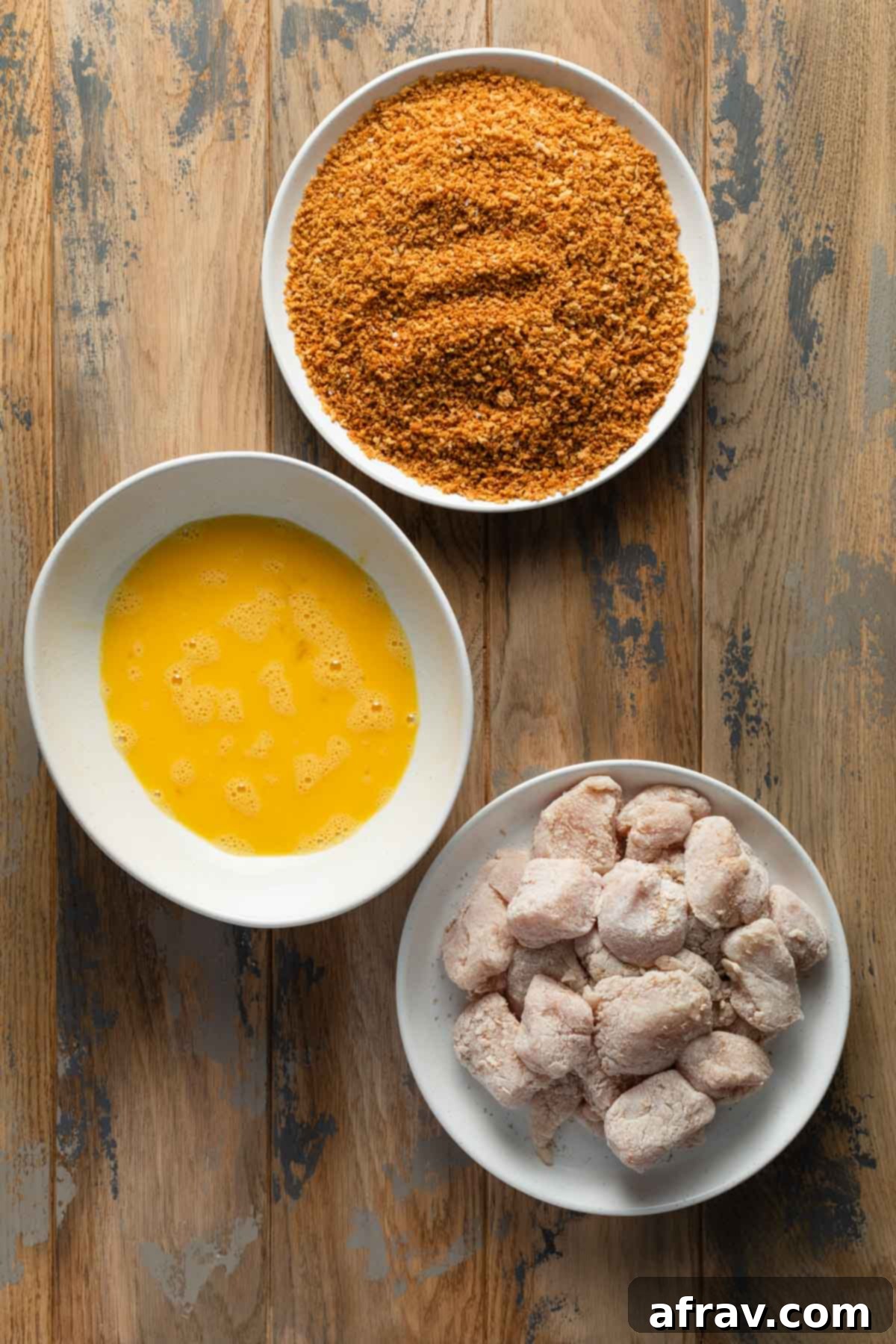 Three shallow dishes: one with floured chicken, one with whisked eggs, and one with seasoned panko crumbs, set up for breading.