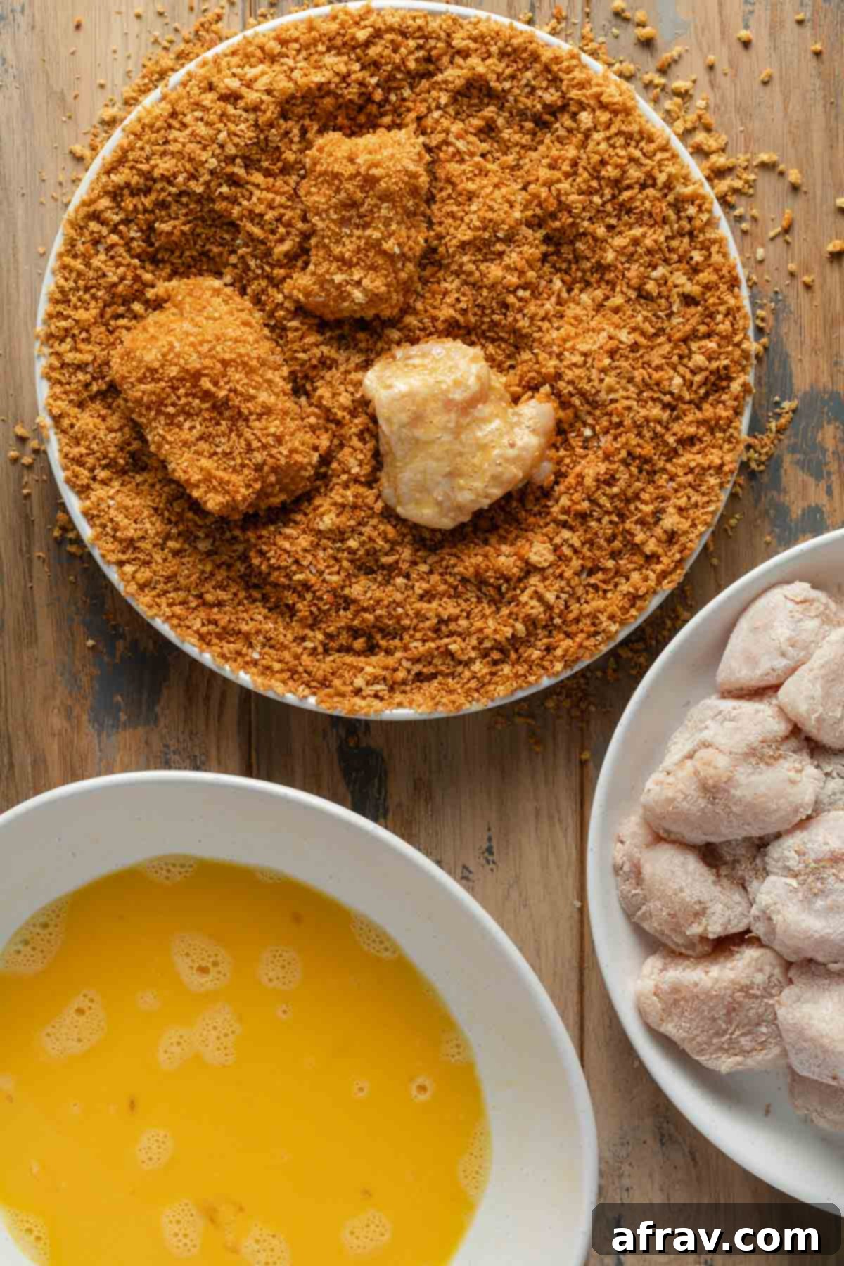 A hand gently pressing panko crumbs onto a chicken piece during the breading process.