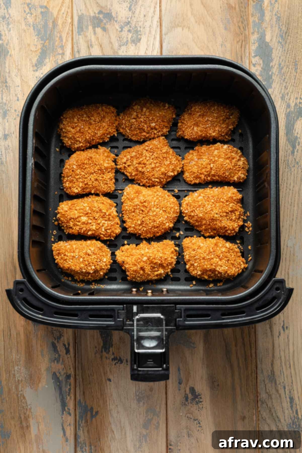 Uncooked breaded chicken pieces arranged neatly in a single layer in an air fryer basket, ready for cooking.