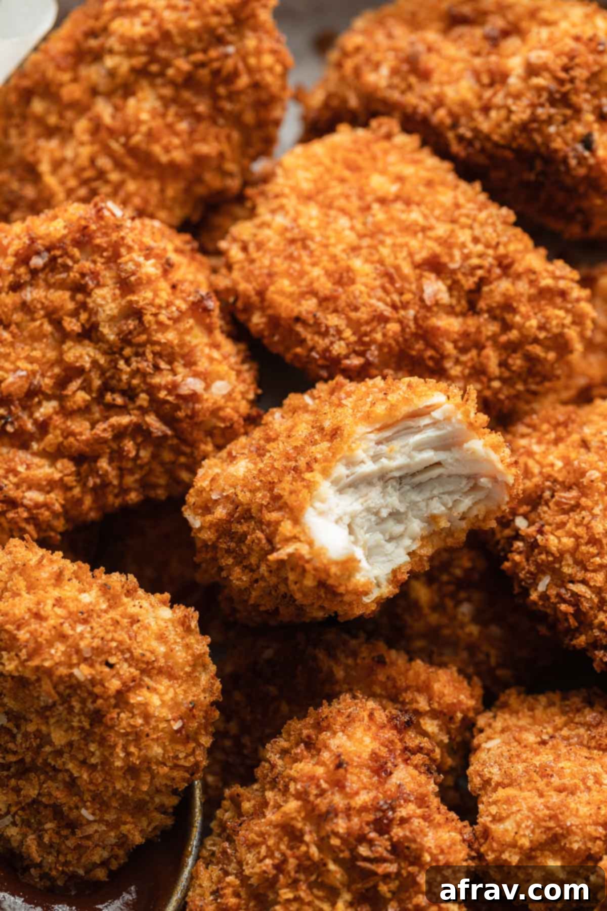 A close-up view of an air-fried chicken nugget with a bite taken out, revealing the juicy interior.