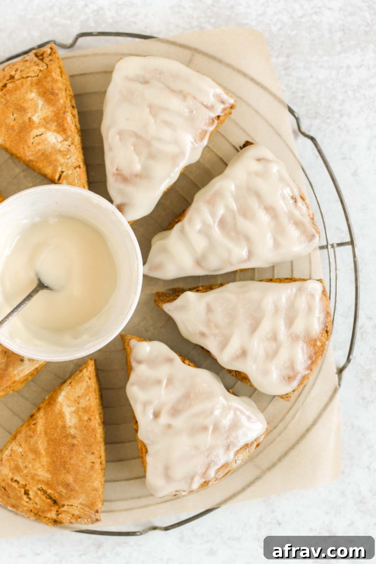 Partially frosted pumpkin scones with a bowl of icing on a round cooling rack.