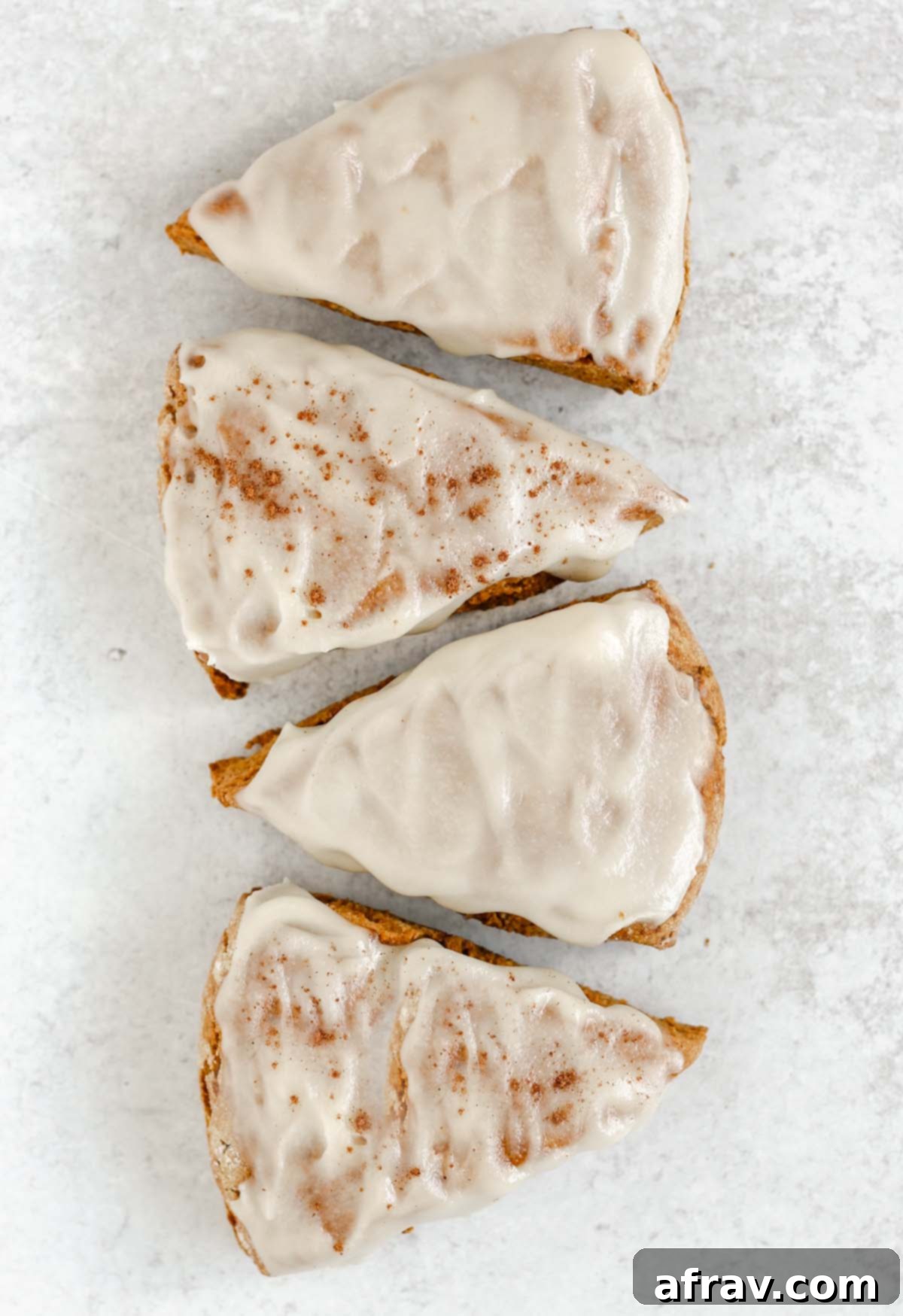 Four frosted pumpkin scones laid out in a line on a gray surface.