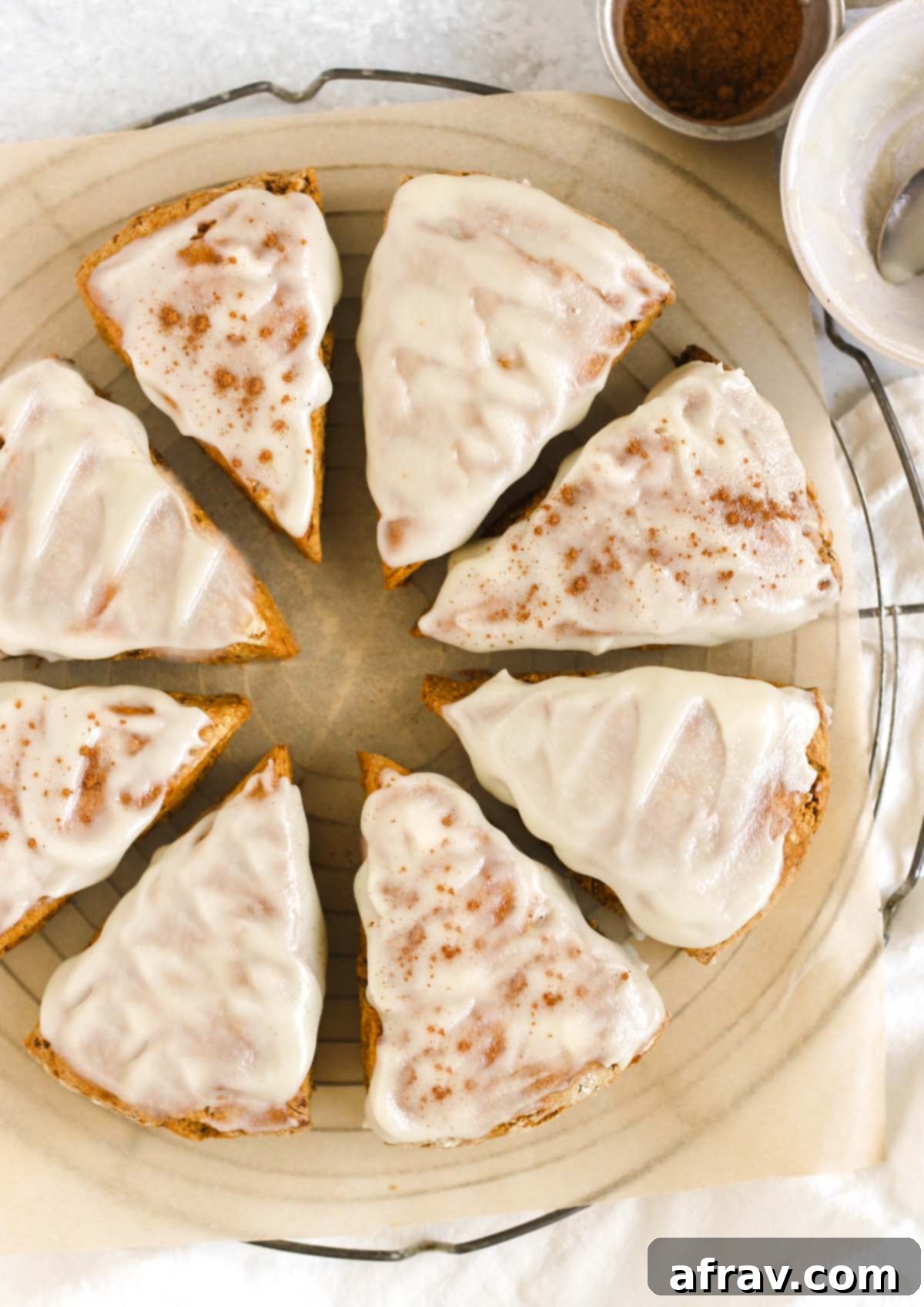 Eight frosted pumpkin scones on a round cooling rack.