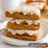 Pumpkin scones stacked 3 high on a plate with a ceramic mug and additional scones in the background.
