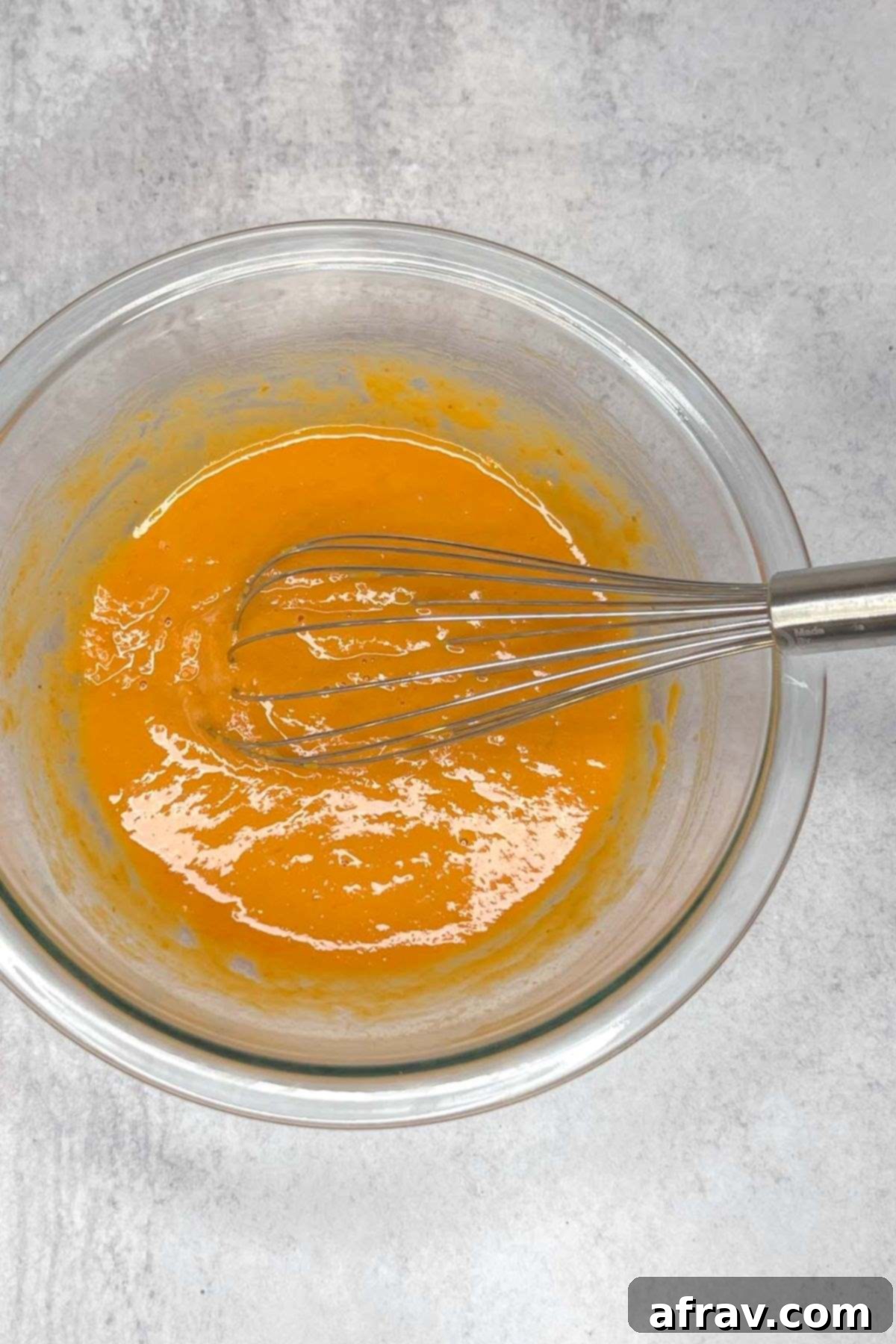 Wet ingredients for pumpkin scones with a whisk in a glass mixing bowl.