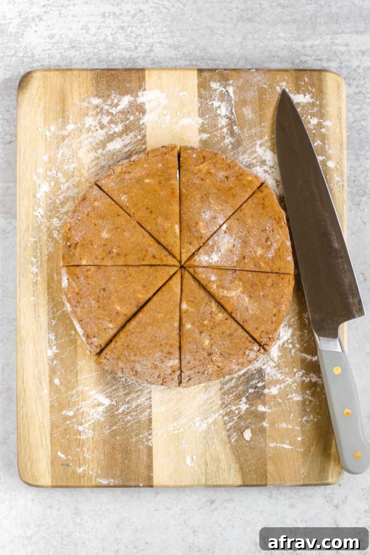 Pumpkin scone dough round cut into 8 wedges on a cutting board.