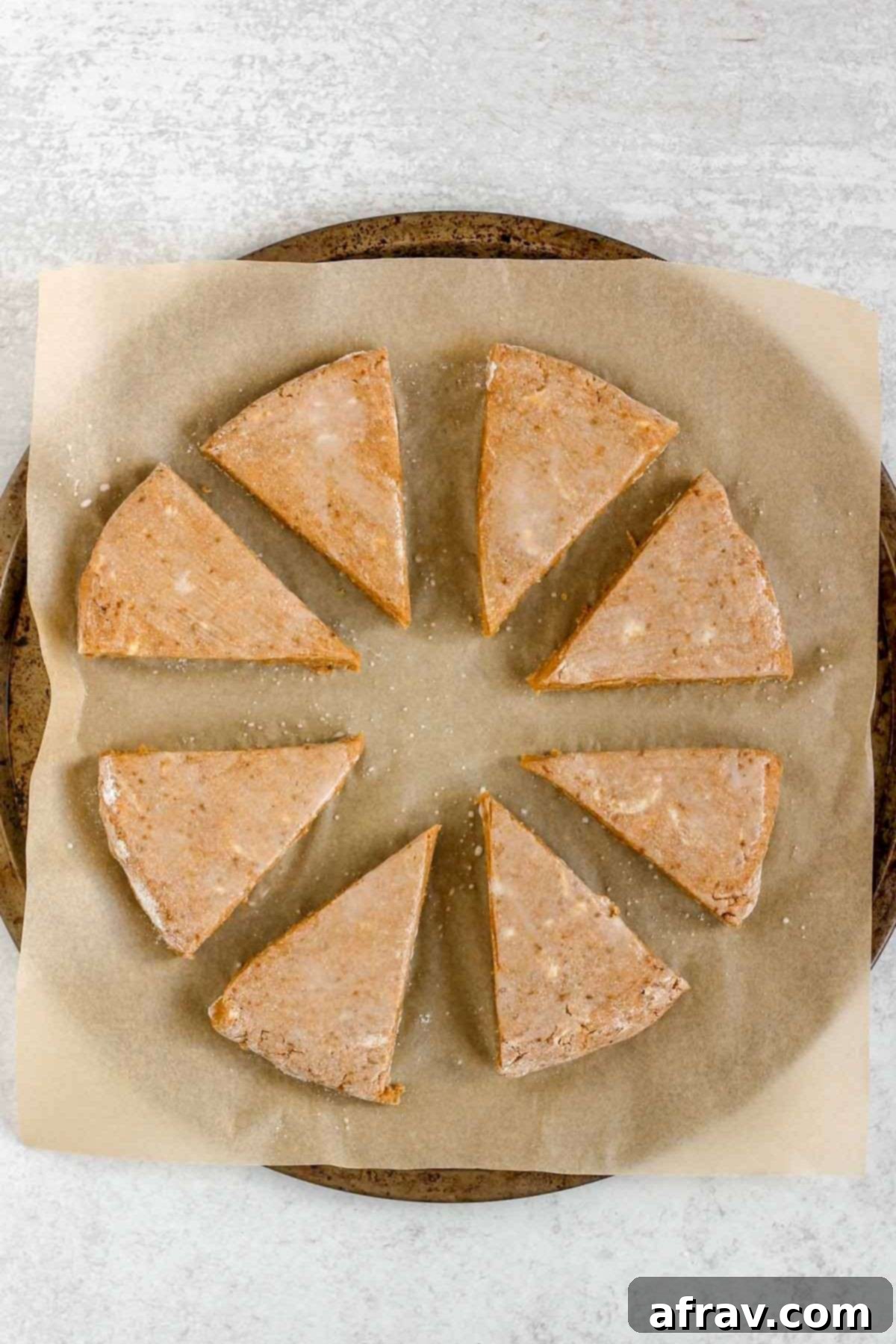 Pumpkin scone dough wedges brushed with milk, arranged on a round baking sheet lined with parchment paper.
