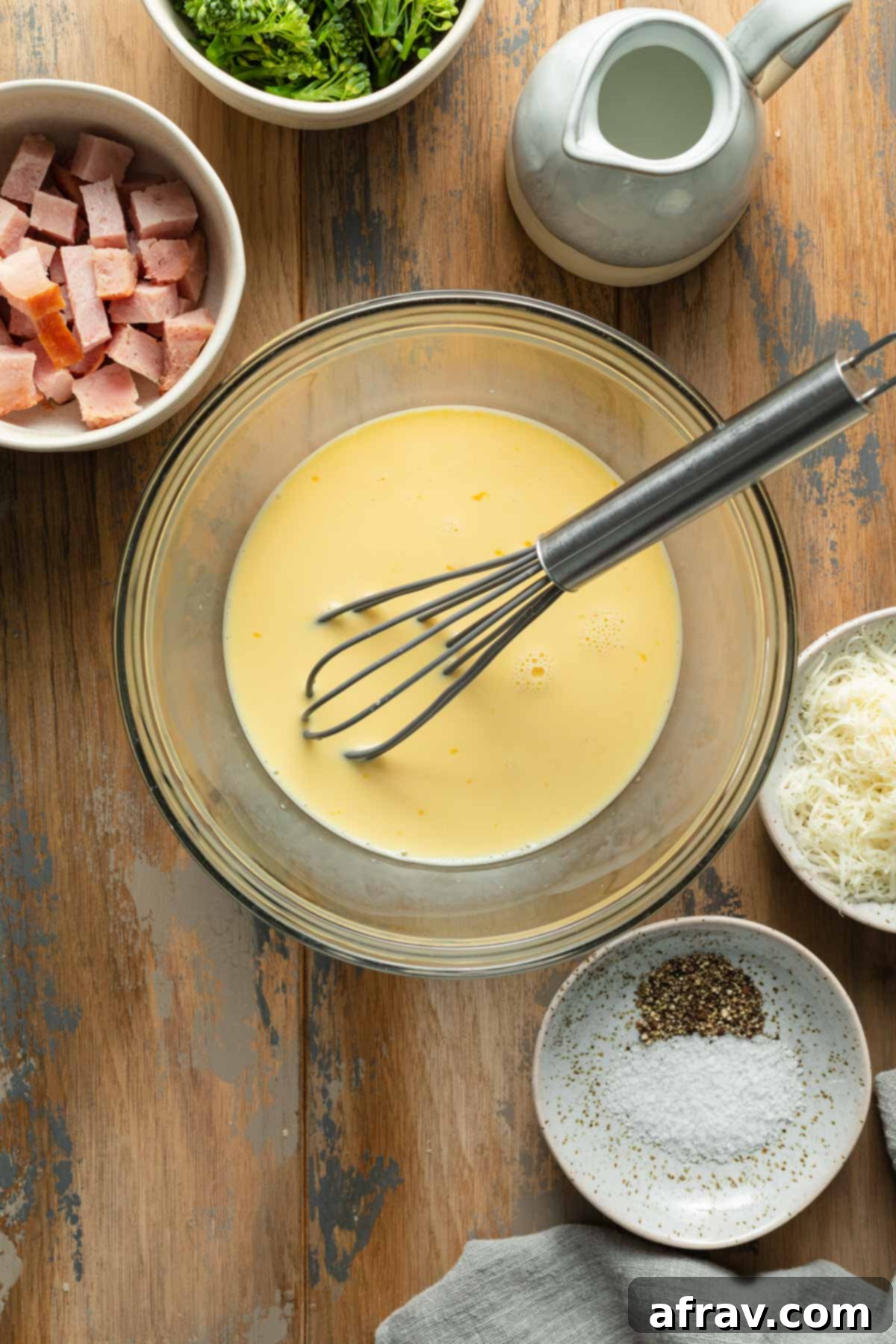 Egg mixture whisked together in a glass bowl with filling ingredients surrounding it.