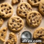 Oat flour chocolate chip cookies arranged on a beige surface next to a measuring cup of flaky sea salt, highlighting their readiness for enjoyment.