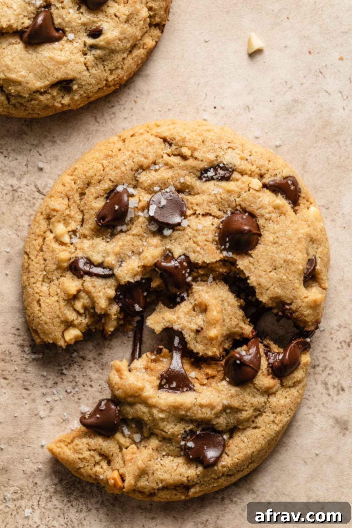 Close up view of a chocolate chip cookie pulled apart, revealing its soft, gooey center with melted chocolate chips, highlighting the perfect texture.