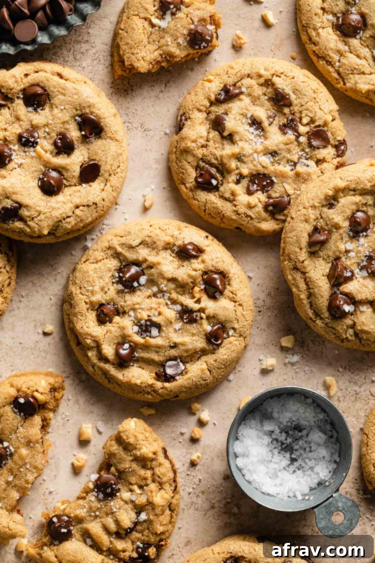 Oat flour chocolate chip cookies artfully arranged on a beige surface, sprinkled with flaky sea salt, highlighting their golden-brown edges.