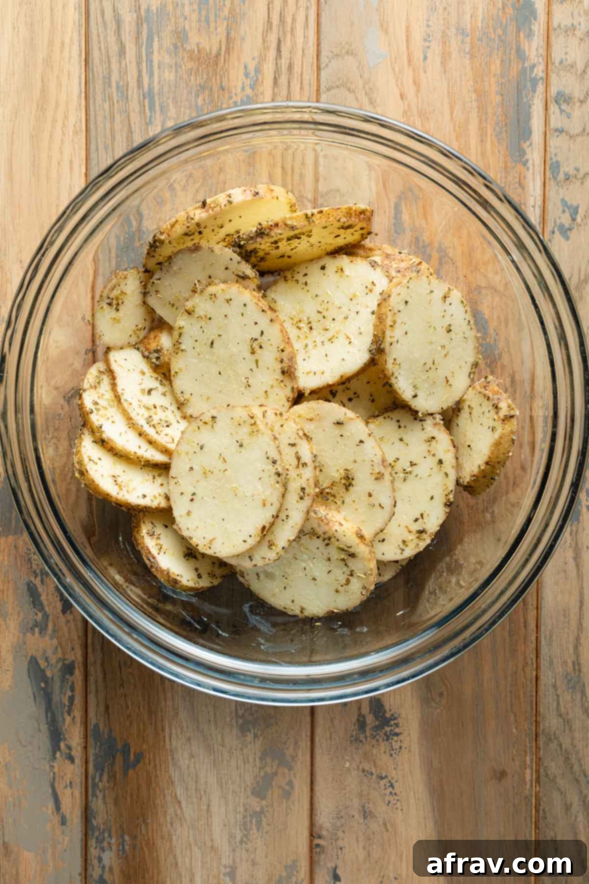 Seasoned potato slices in a large glass bowl.