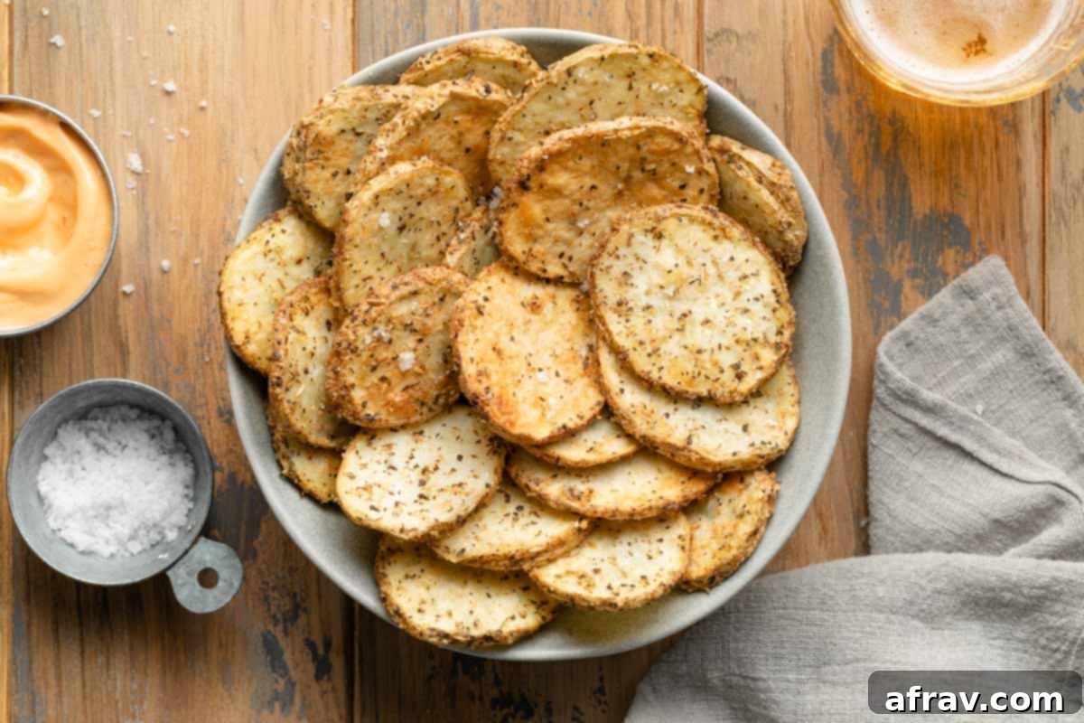 A bowl of crispy potato slices next to dishes of salt and dip and a beverage.