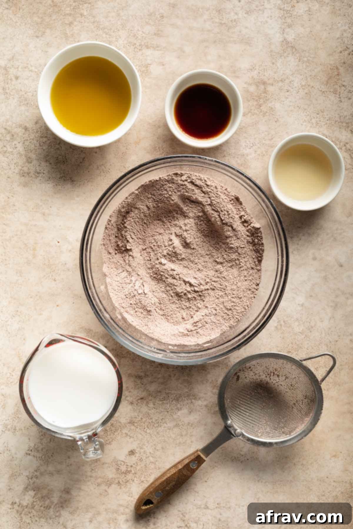 Dry ingredients sifted together in a glass bowl with the wet ingredients and a sifter surrounding it.