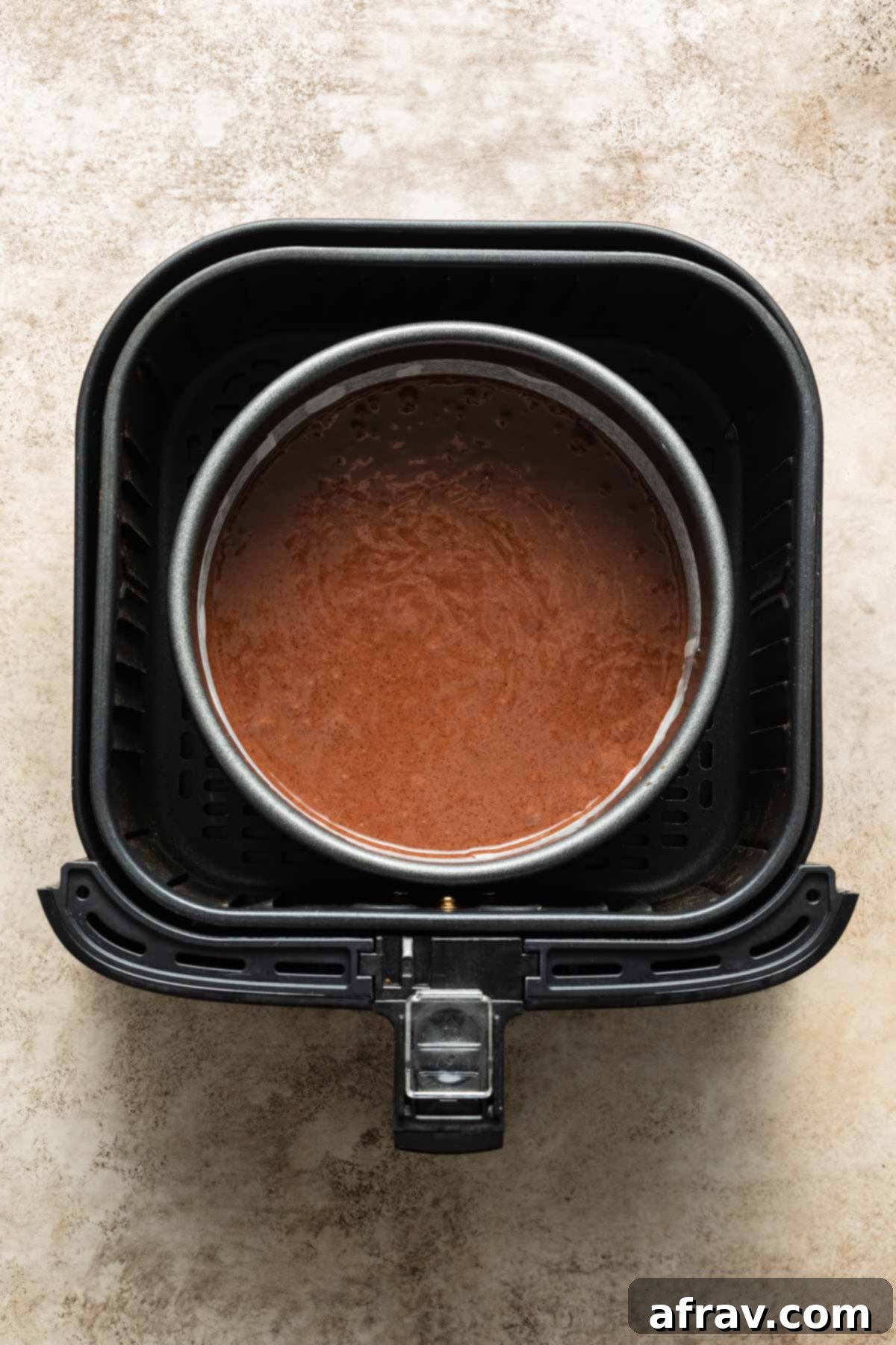 Overhead view of chocolate cake batter in a round pan inside an air fryer basket.