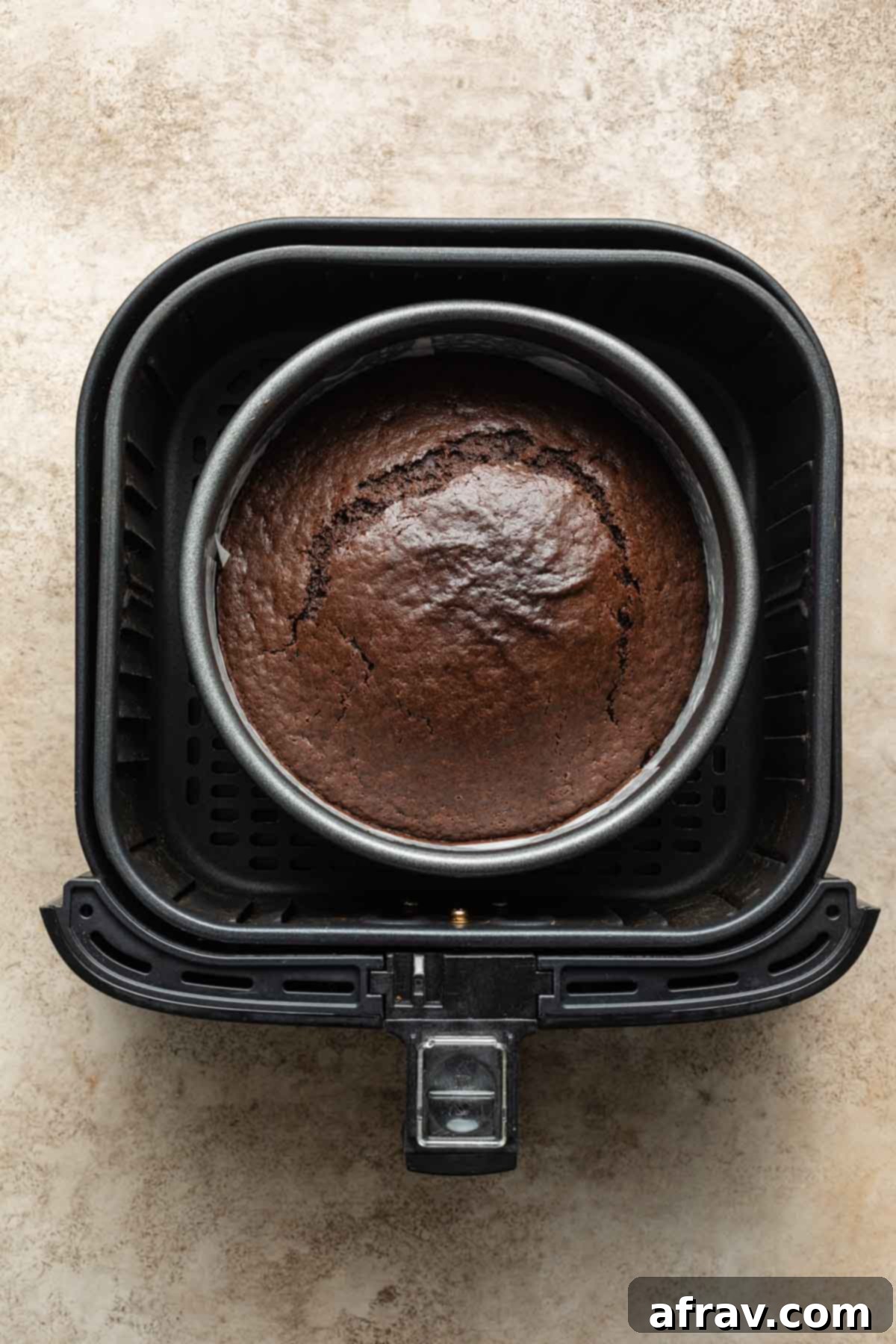 Overhead view of a baked chocolate cake in a round pan inside an air fryer basket.