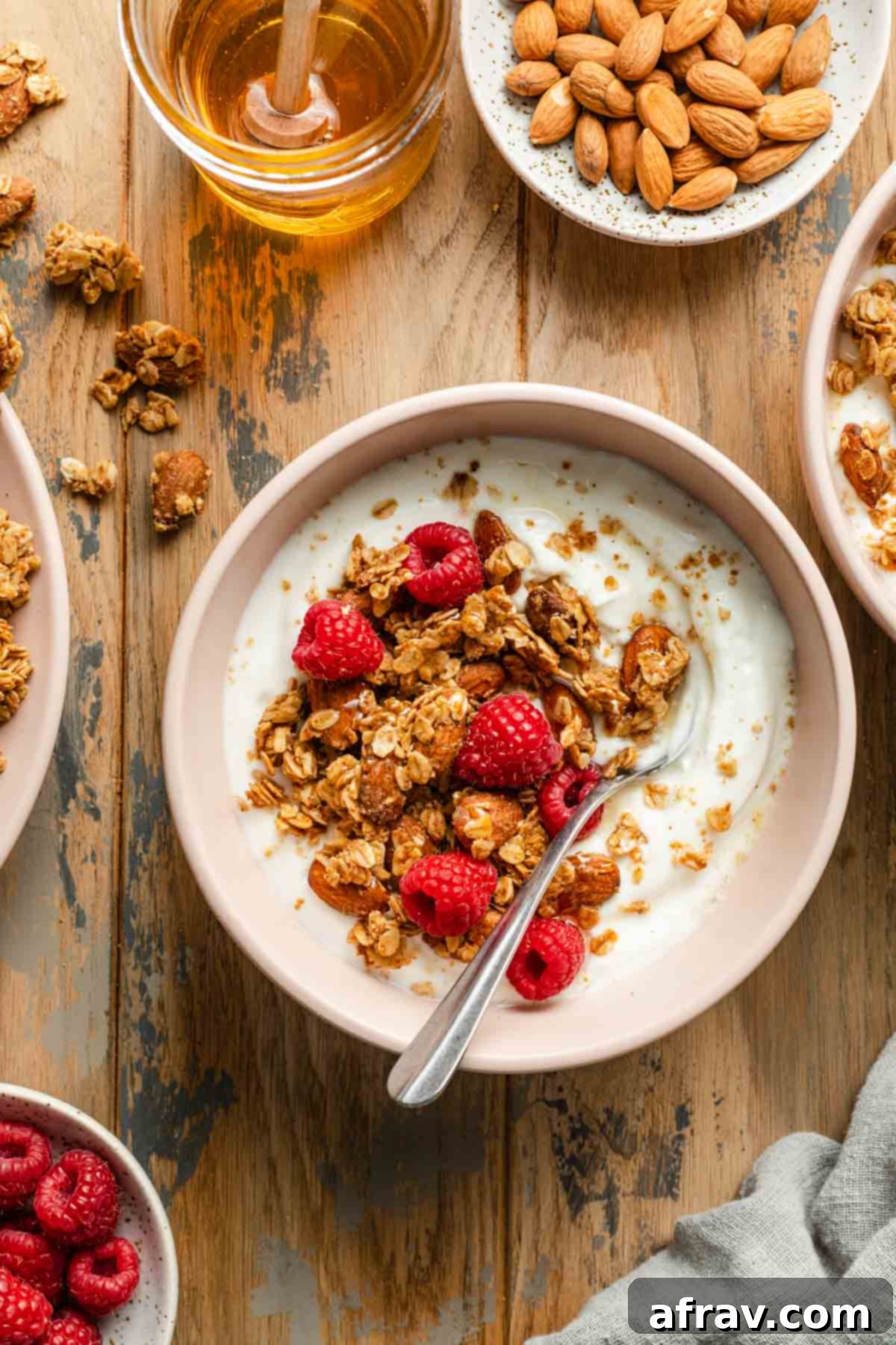 Honey almond granola in a pink bowl with yogurt and raspberries on top, showing crunchy clusters.