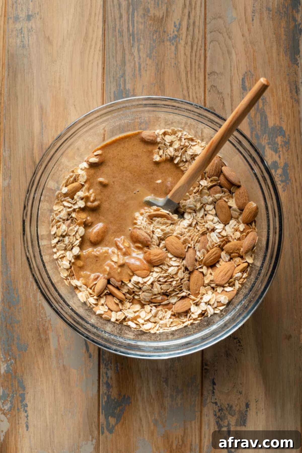 Overhead view of granola ingredients added to a glass bowl, showcasing the oats and almonds.