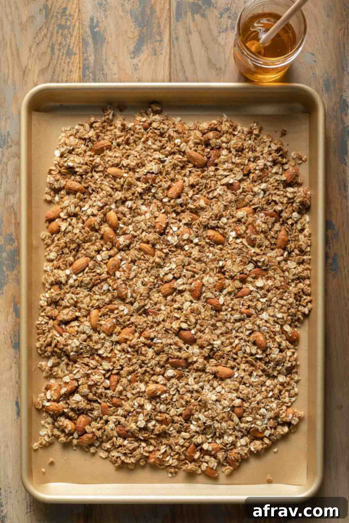 Granola mixture spread out on a parchment paper lined baking sheet, ready for baking.