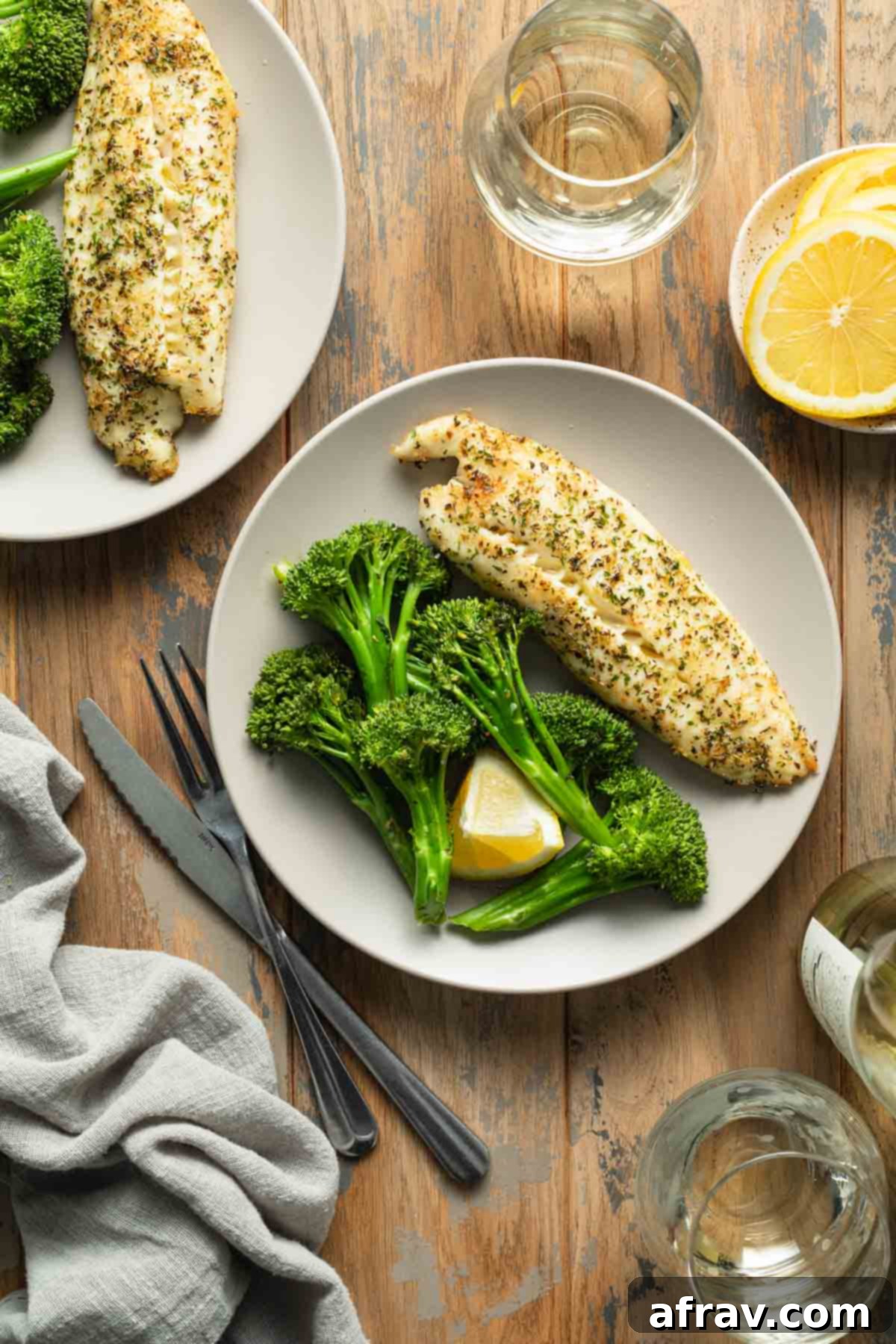 Two plates of air fryer tilapia and roasted broccoli arranged on a table, showcasing a healthy dinner.