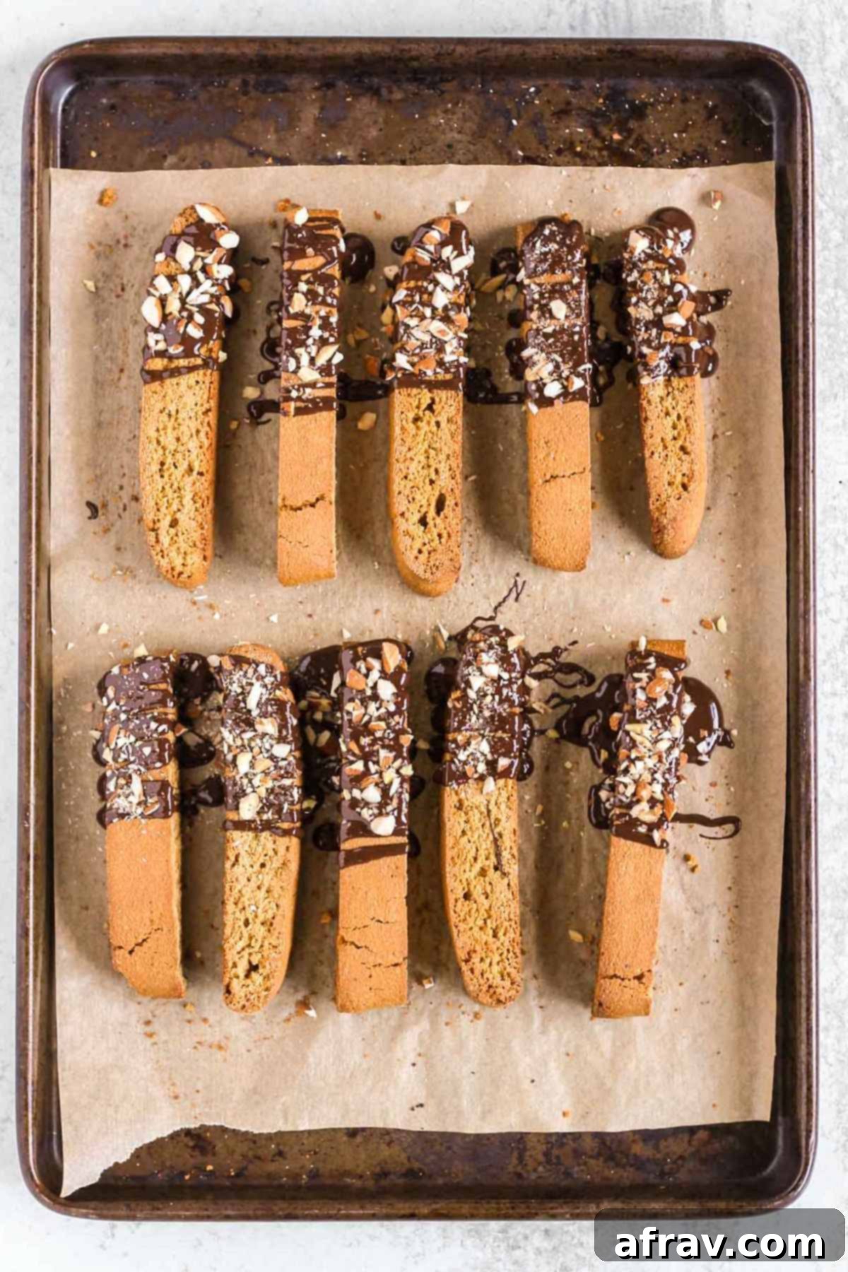 Biscotti cookies drizzled with chocolate and topped with almond pieces on a parchment paper lined baking sheet.