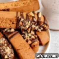 Biscotti drizzled with chocolate and almond pieces stacked on a plate.