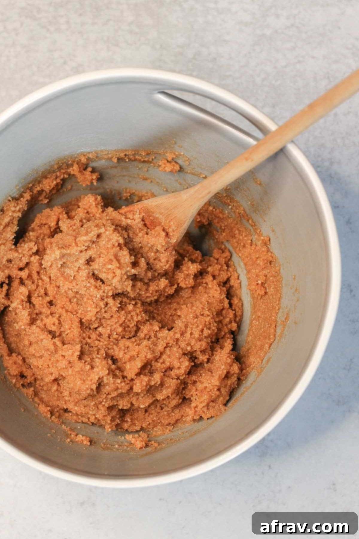 Almond flour biscotti dough with a wooden spoon in a gray mixing bowl.