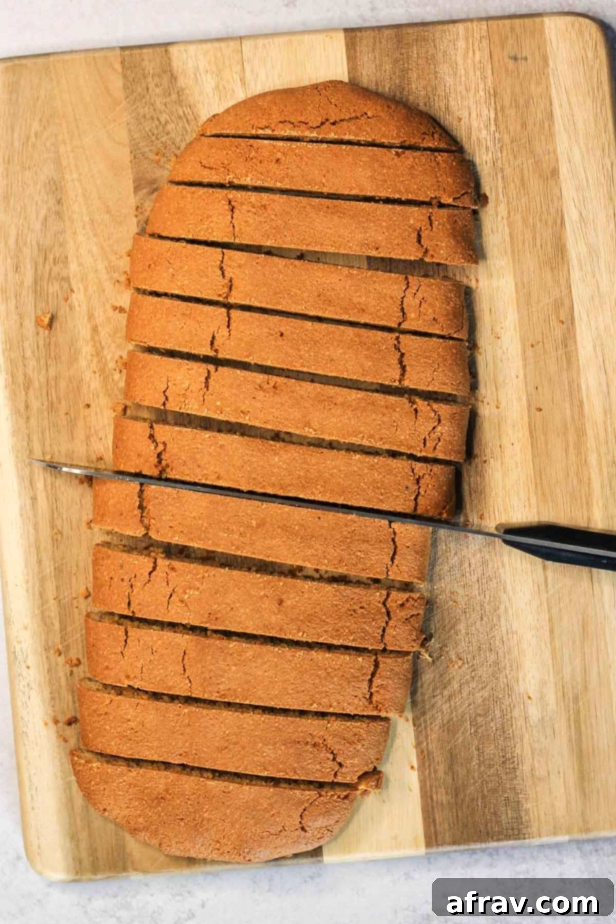 Biscotti loaf being cut on a cutting board after being baked the first time.