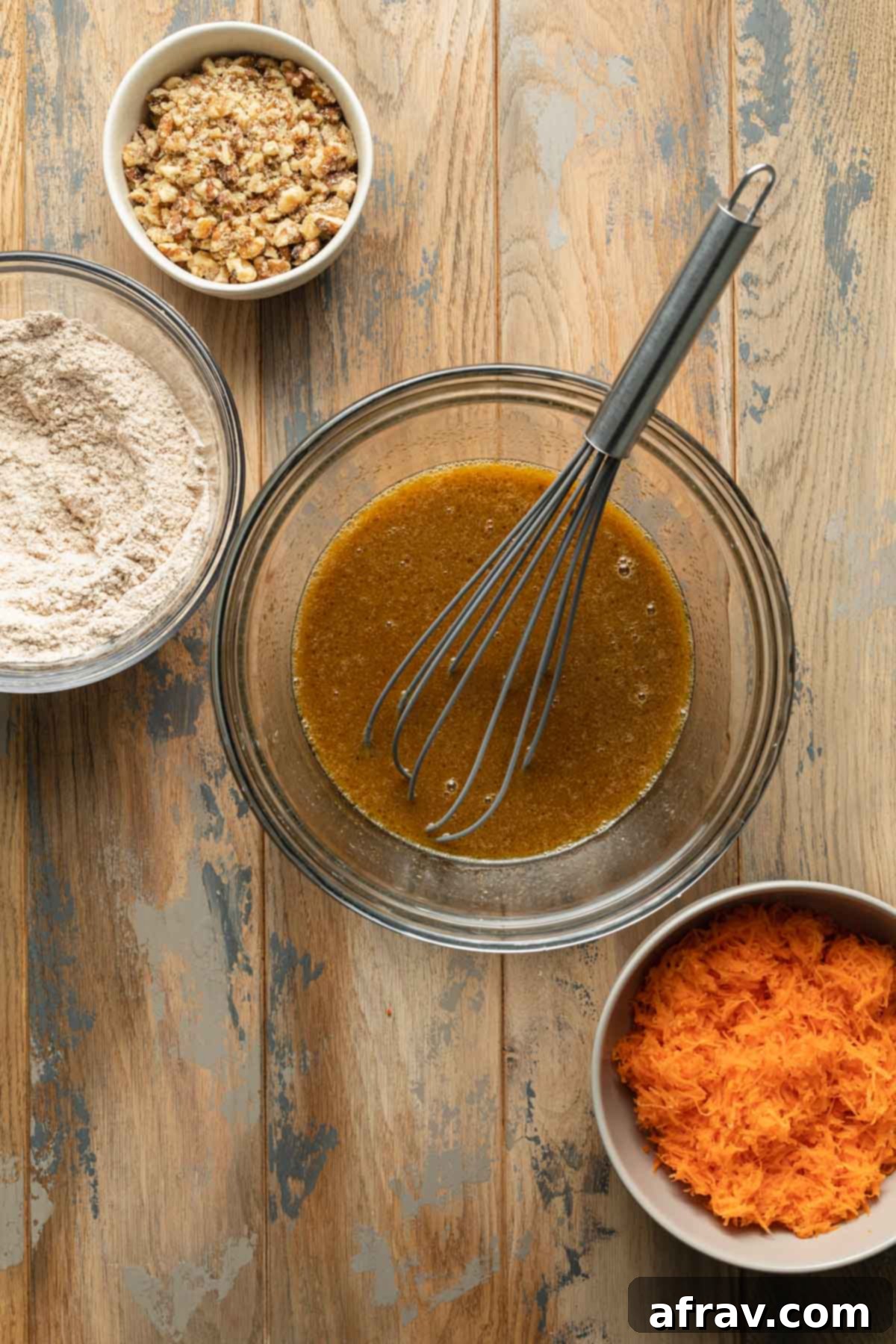Wet ingredients for the carrot cake, including sugars, milk, oil, egg, and vanilla, whisked together in a clear glass bowl.