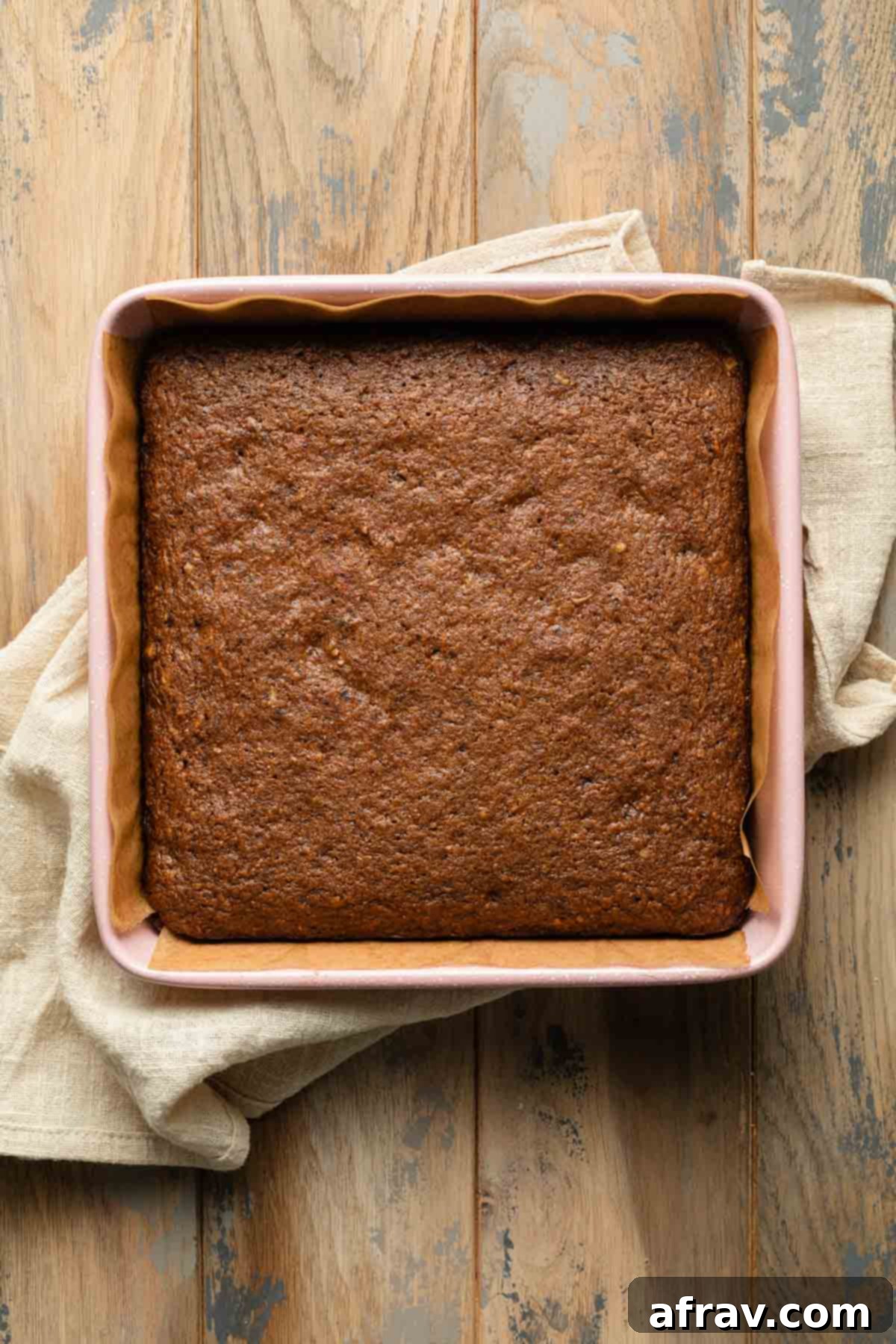 A freshly baked small carrot cake cooling in its pink square baking pan on a wire rack, steam gently rising.