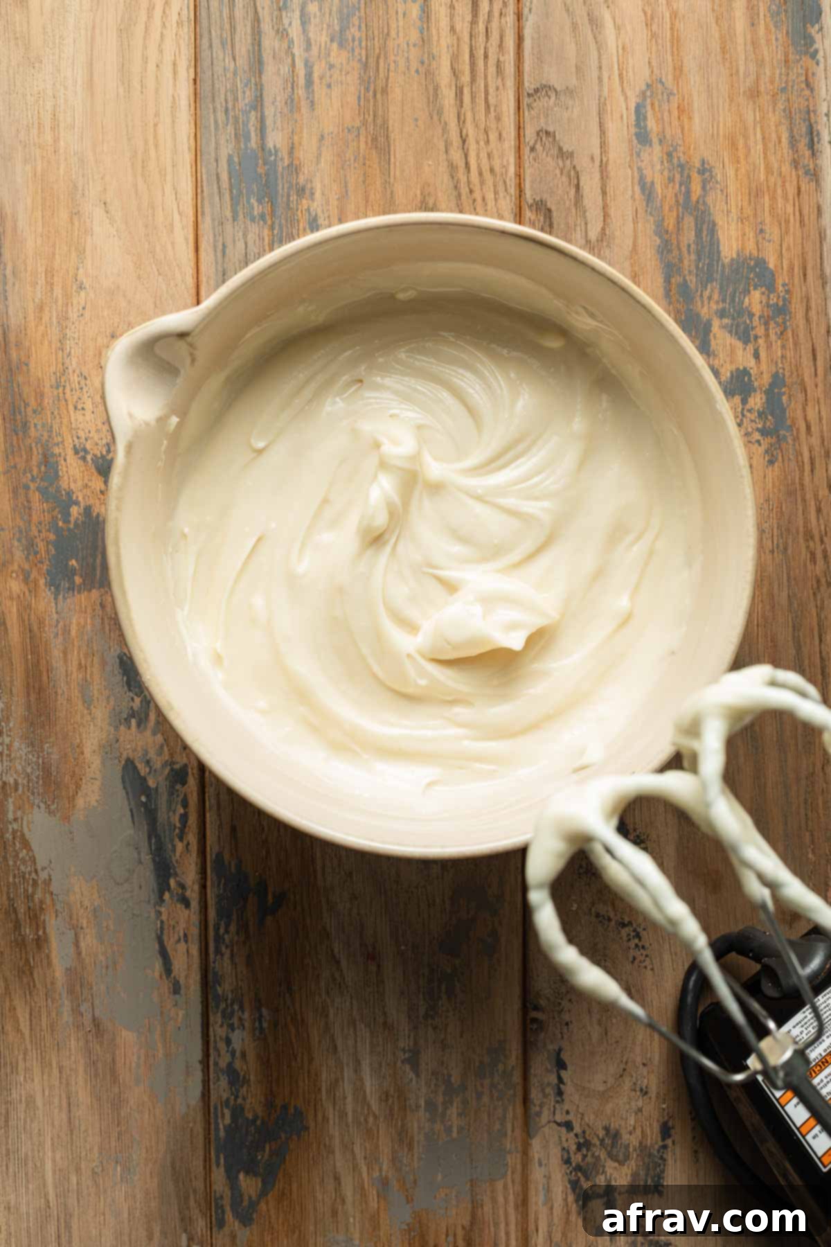 An overhead view of creamy, white homemade cream cheese frosting swirled in a glass mixing bowl, ready for application.