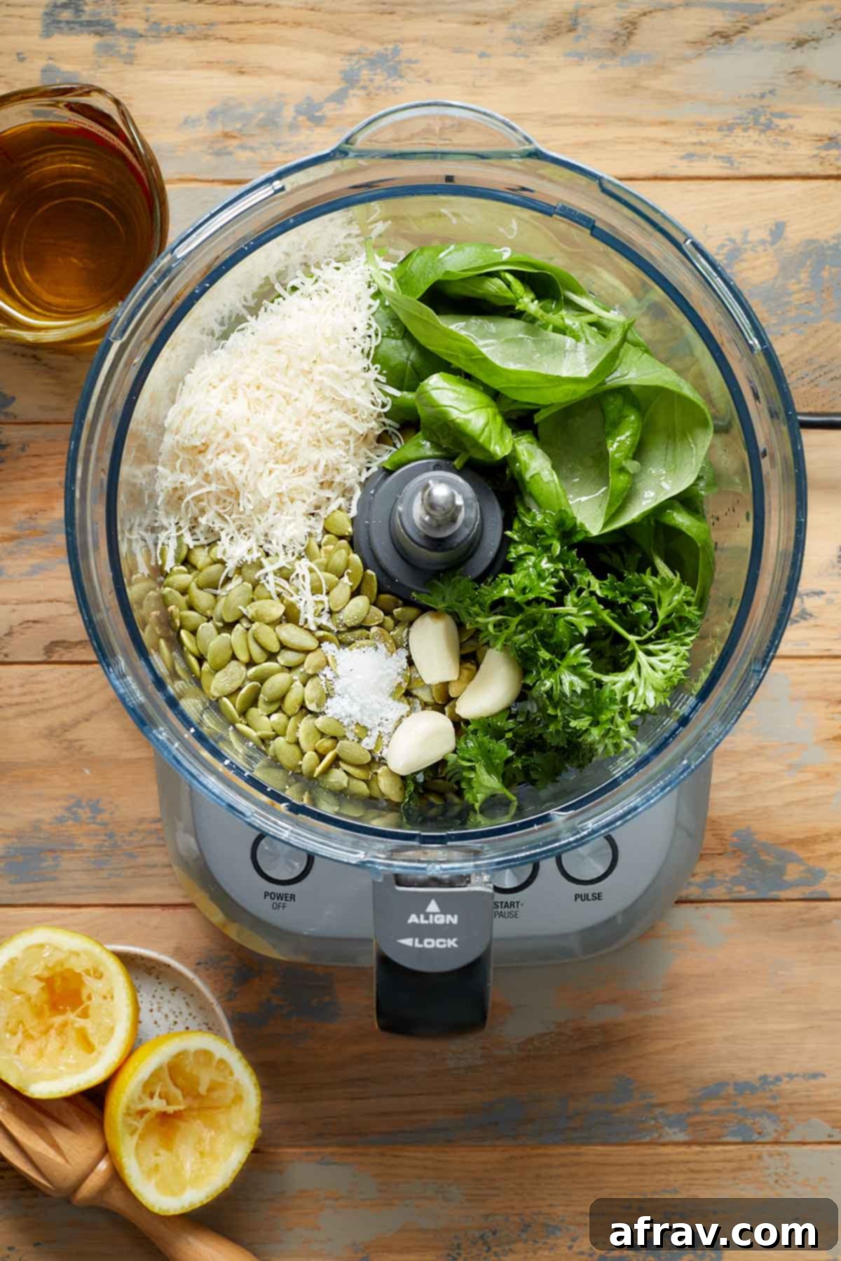 Pesto ingredients in a food processor with olive oil and squeezed lemons on the side, ready for blending.
