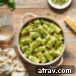 Pasta with pumpkin seed pesto in a bowl with a glass of wine, bread, pumpkin seeds and parmesan cheese surrounding it, illustrating a complete meal.