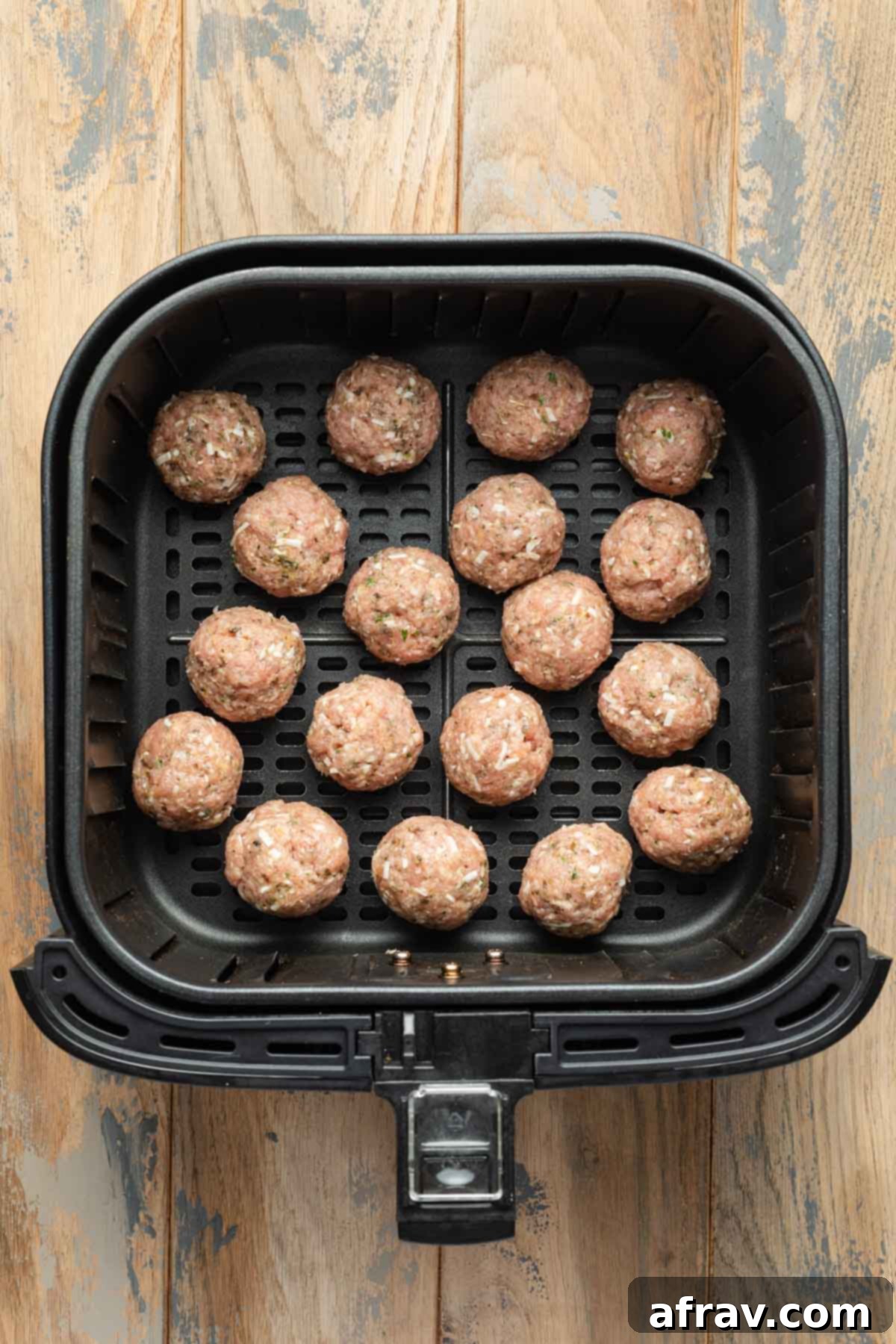 Uncooked meatballs in an air fryer basket.