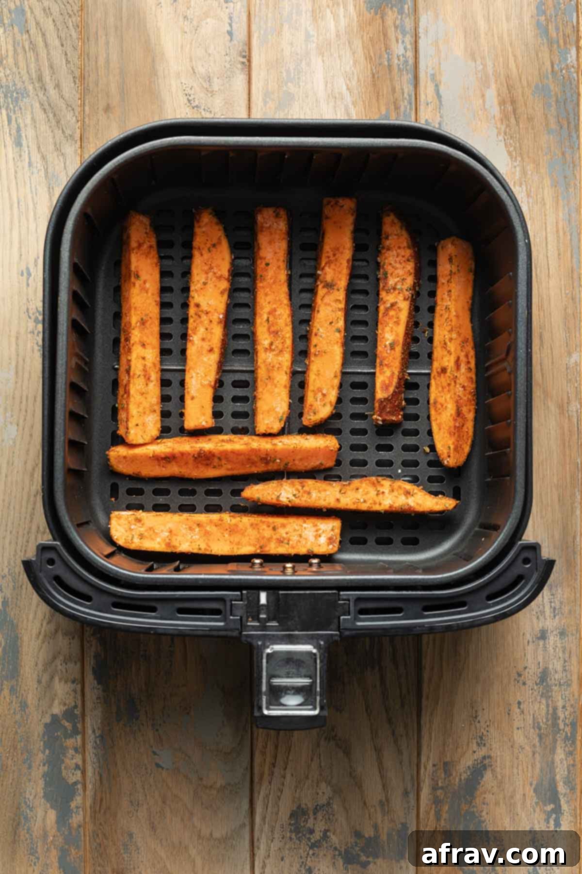 Seasoned sweet potato wedges arranged in a single layer in an air fryer basket.