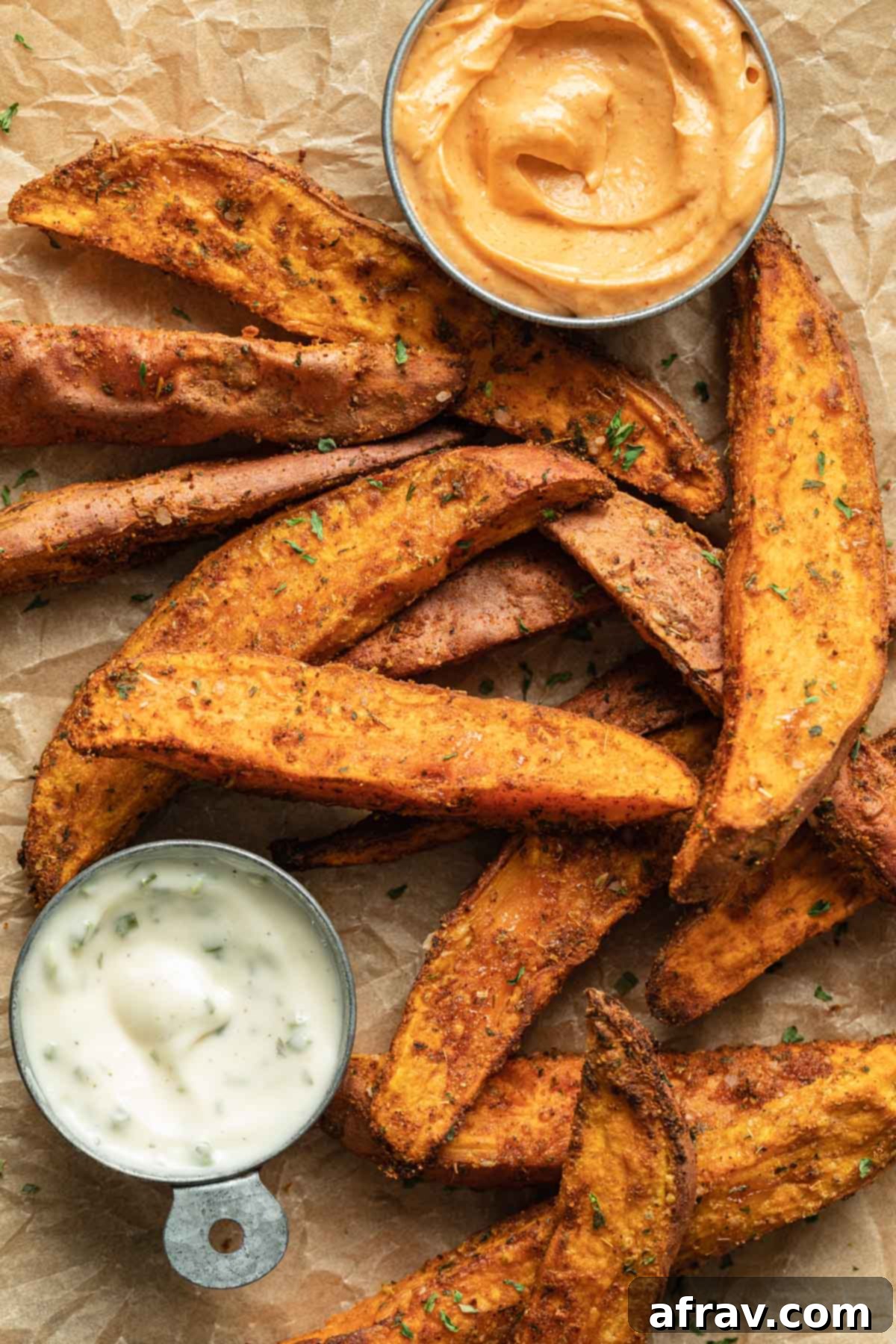 Air fryer sweet potato wedges arranged on parchment paper with a side of ranch dip.