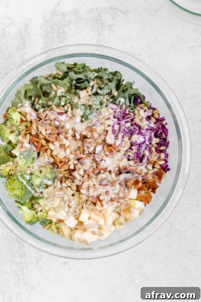 The creamy dressing has just been poured over the broccoli kale salad ingredients in a mixing bowl, ready to be tossed.