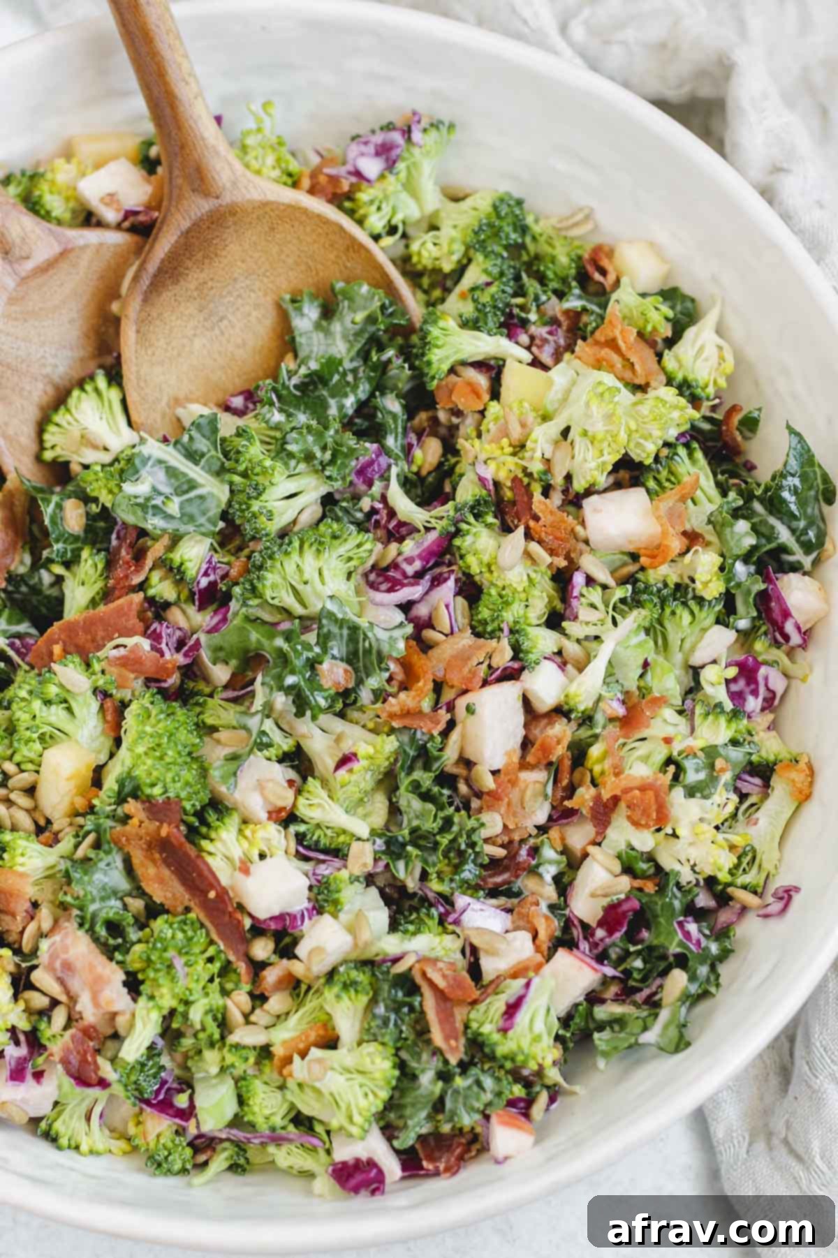 Close-up of the finished healthy broccoli kale salad in a white bowl, served with wooden salad utensils.