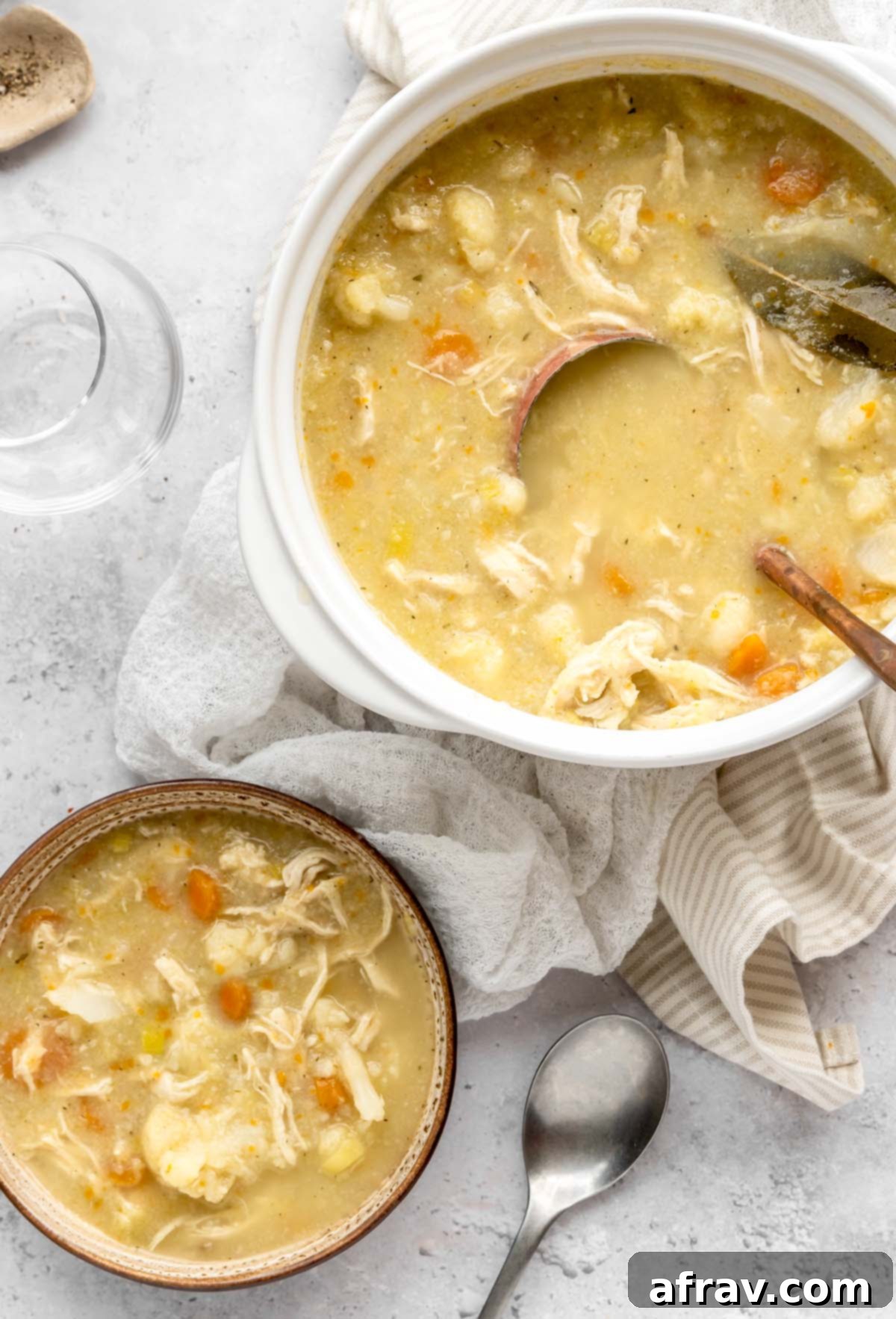 A bowl and larger soup crock next to each other filled with creamy chicken and cauliflower soup.