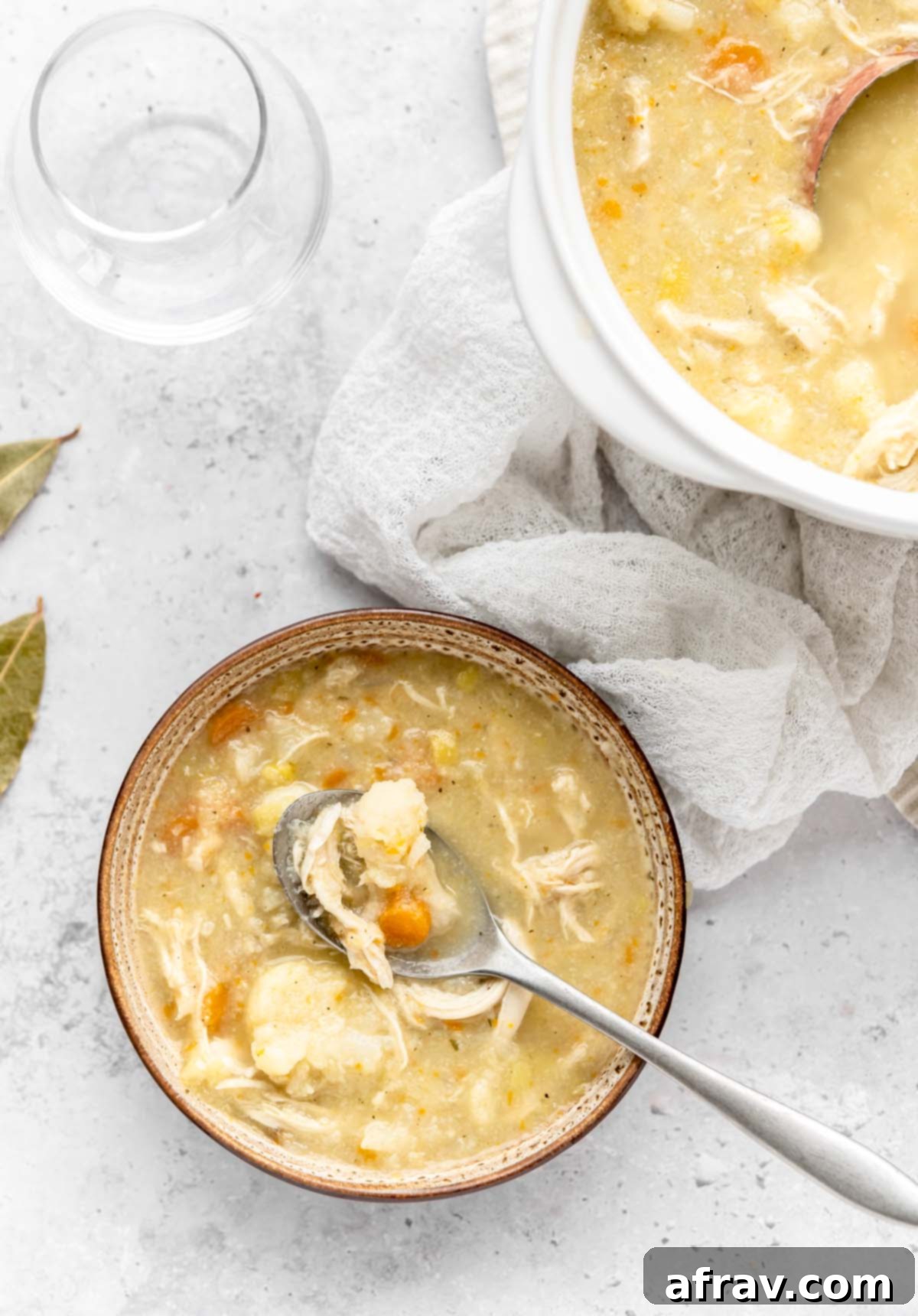 A bowl of chicken cauliflower soup with a spoonful being scooped out and a soup crock filled with soup in the background.