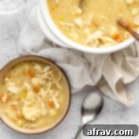 A bowl and larger soup crock next to each other filled with creamy chicken and cauliflower soup.