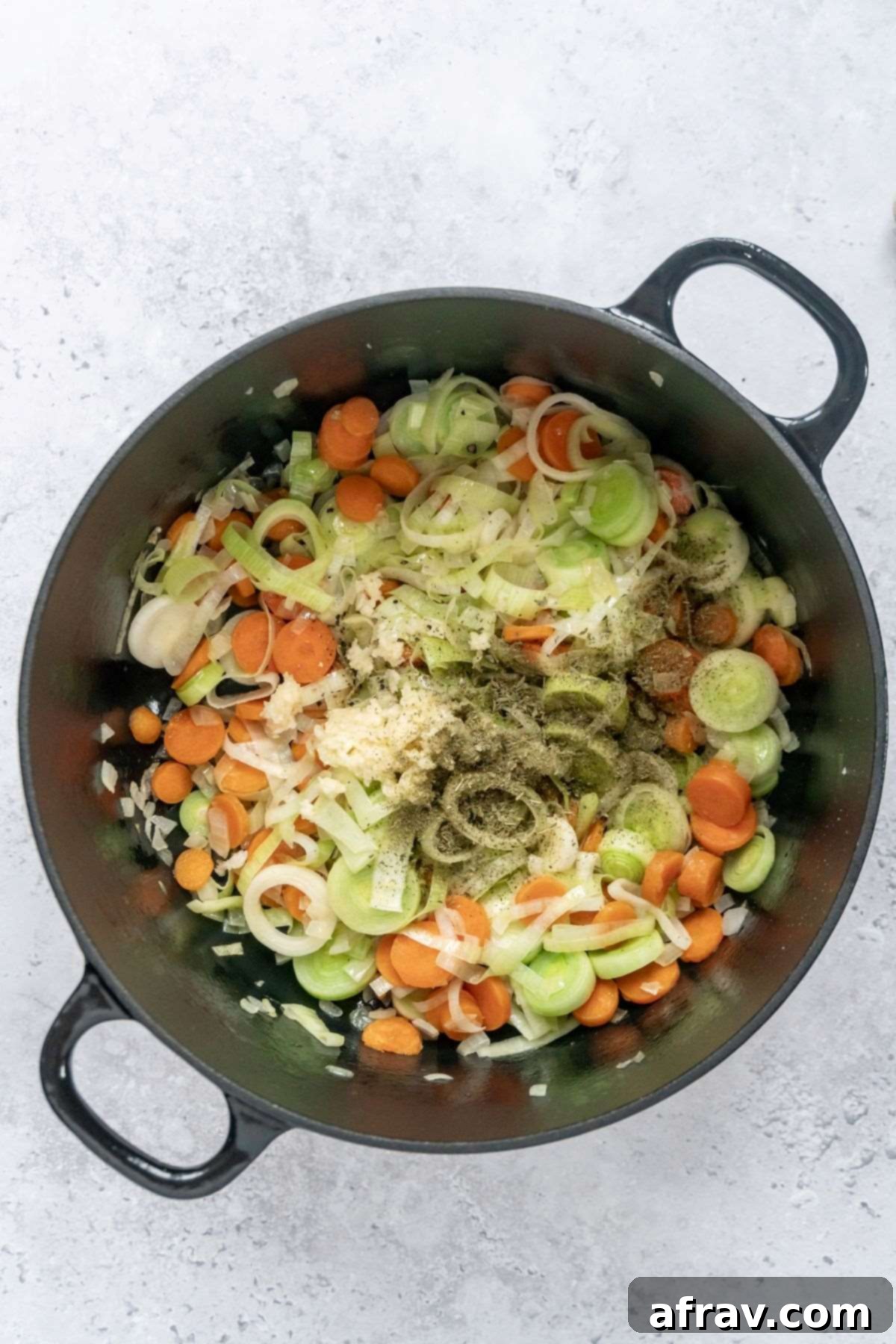 Sautéed carrots, onions, and leeks sprinkled with thyme, salt, and pepper in a black stock pot.