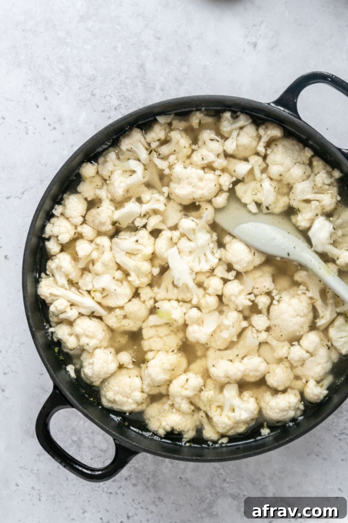 Cauliflower florets in a large black stock pot topped with broth.