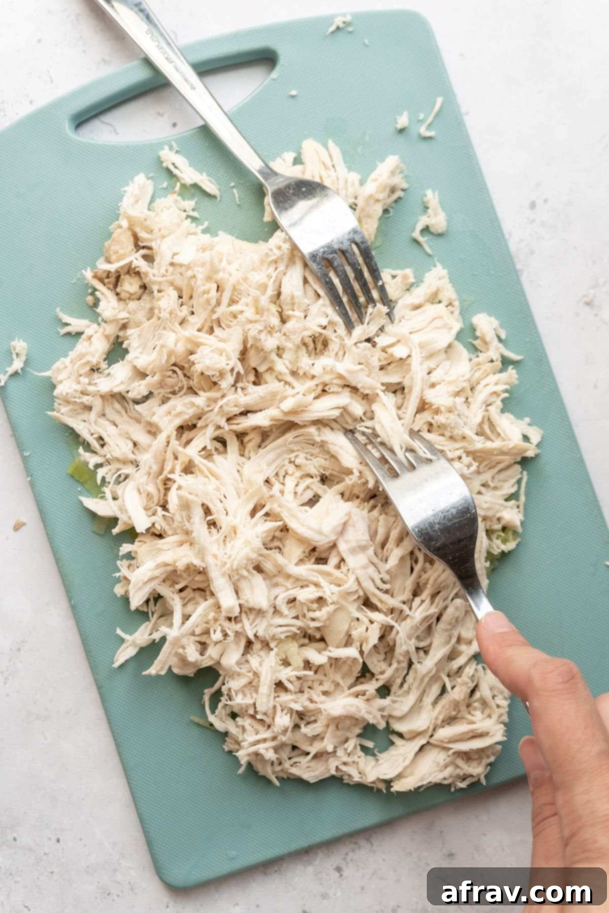 Two forks shredding chicken on a cutting board.