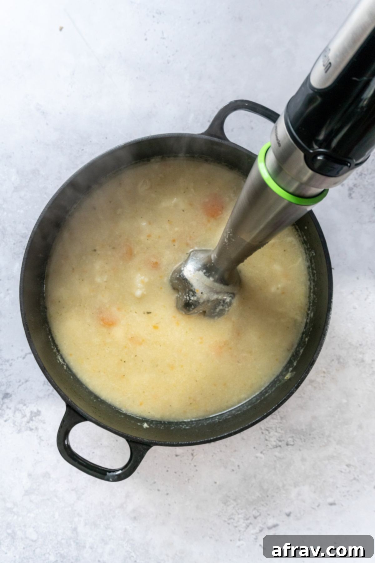 Immersion blender blending soup in a black stock pot.
