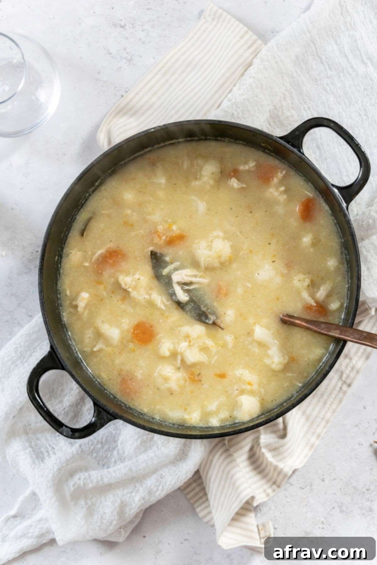 Creamy chicken and cauliflower soup with a copper ladle in a black stock pot.