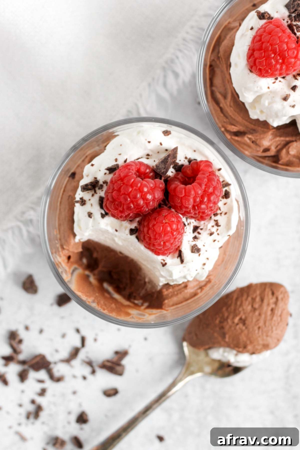 Chocolate mousse topped with whipped cream and raspberries in a small serving dish with a spoonful taken from the dish.