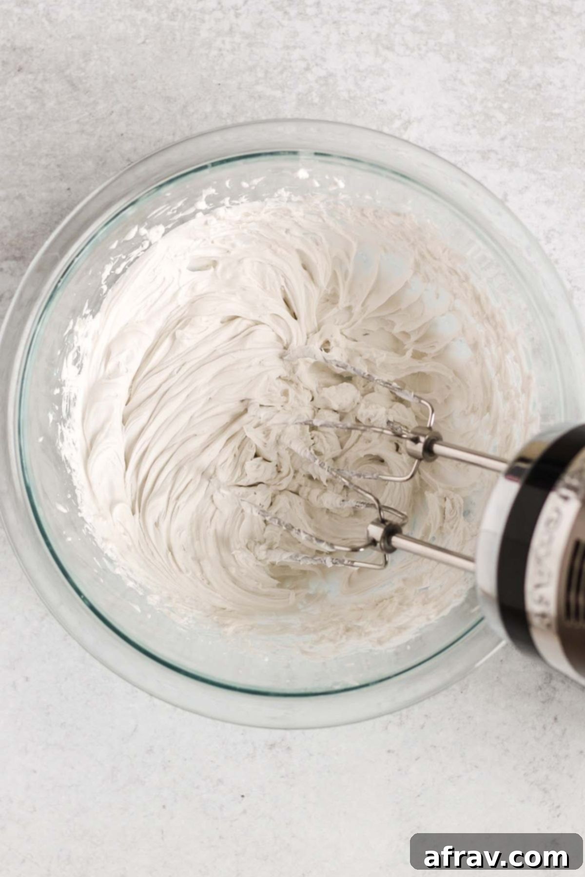 Whipped coconut cream with a hand-held blender in a mixing bowl.