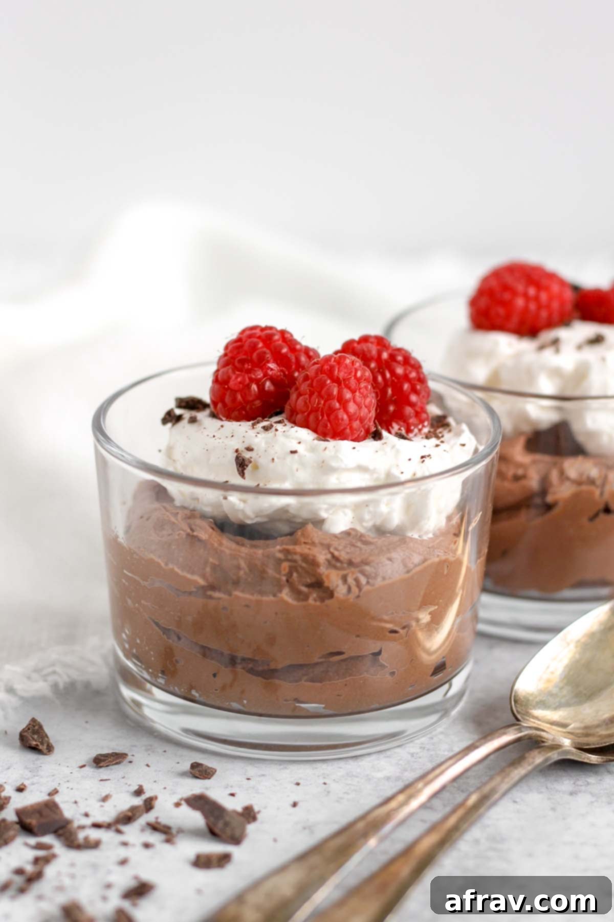 Single serve glass dish filled with chocolate mousse topped with whipped cream and raspberries.