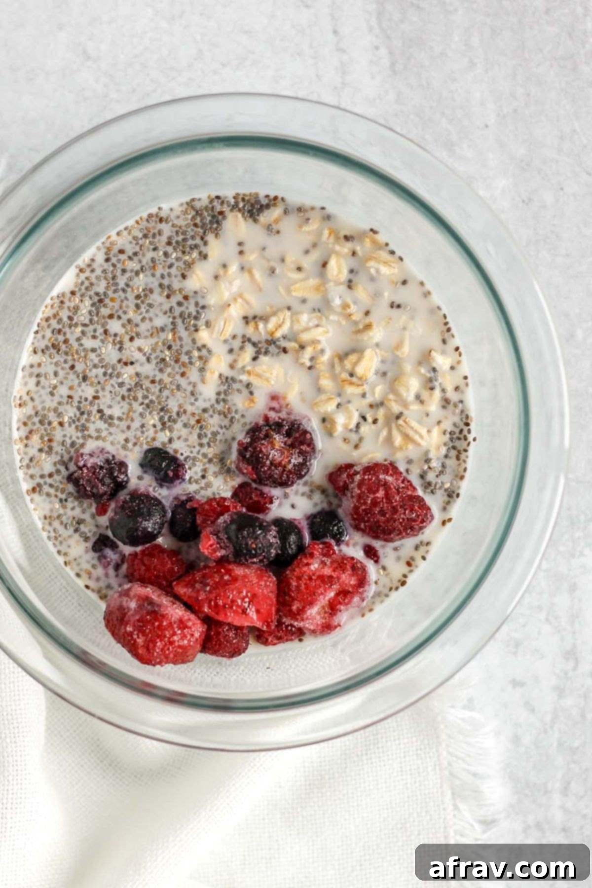 Mixing bowl with oats, milk, chia seeds, and frozen mixed berries.